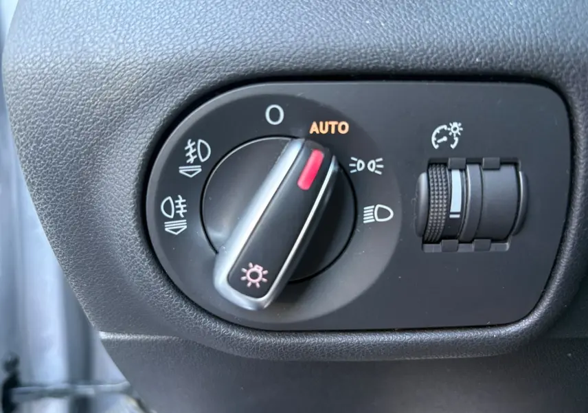 Gros plan sur le bouton de commande des phares avec réglage automatique dans une Audi A1 Sportback grise toit noir.
