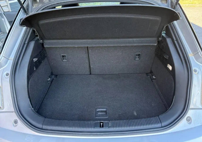 Coffre ouvert d’une Audi A1 Sportback grise, vue arrière, montrant l’espace de rangement vide et la moquette noire.