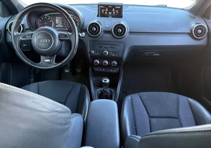 Vue intérieure avant de l'Audi A1 Sportback 1.4 TFSI S-Line 2014, volant sport, écran GPS et levier de vitesses manuel.