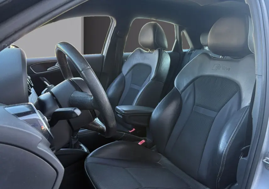 Vue intérieure côté conducteur de l'Audi A1 Sportback 1.4 TFSI S-Line 2014, sièges sport noirs avec logo S-Line visibles.