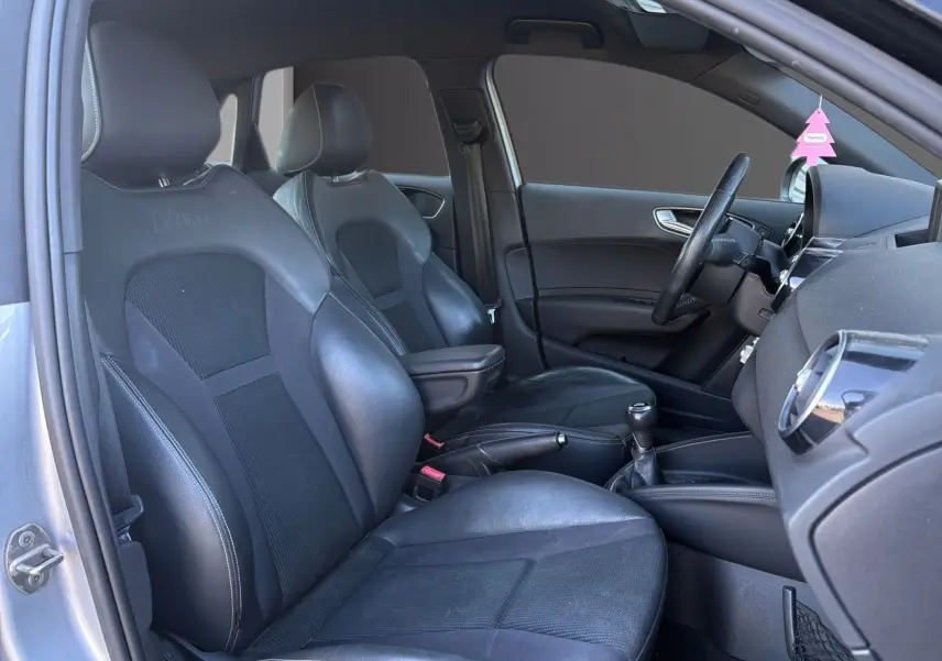 Vue intérieure côté conducteur de l'Audi A1 Sportback 1.4 TFSI S-Line avec sièges sport noirs et accoudoir central.