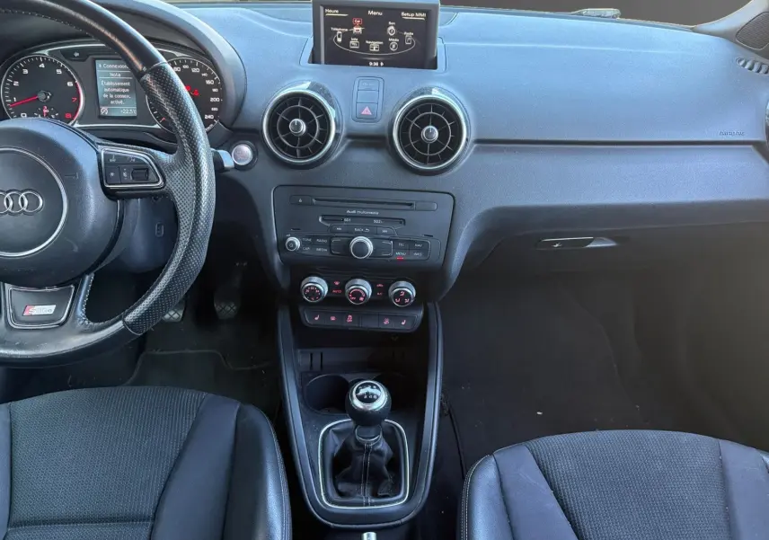Vue intérieure de l'Audi A1 Sportback 1.4 TFSI 2014, tableau de bord noir avec volant sport et levier de vitesse manuel.