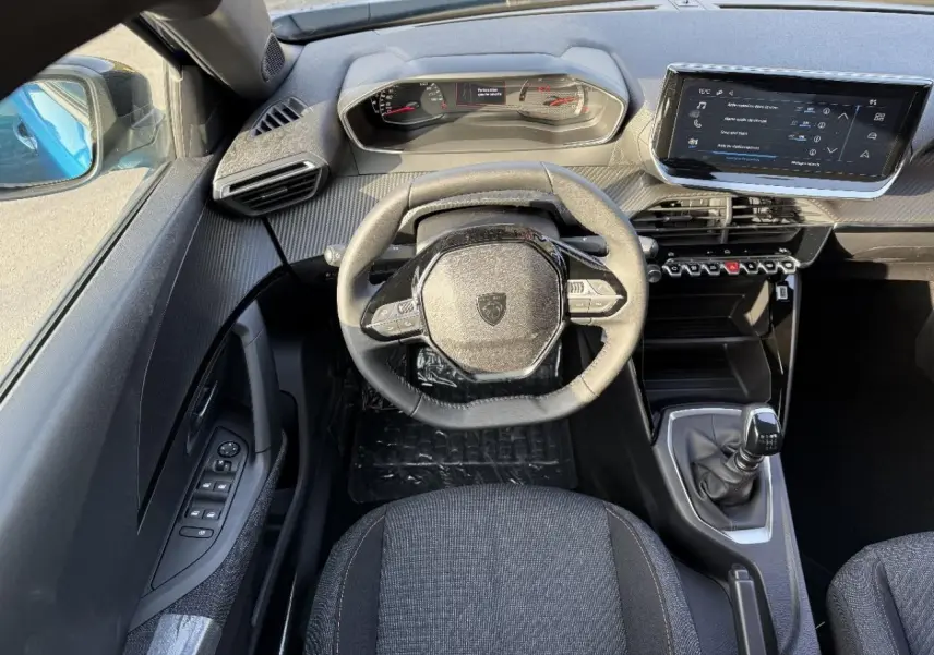 Vue intérieure du poste de conduite du Peugeot 2008 2025 bleu obsession, avec volant compact et boîte manuelle visible.