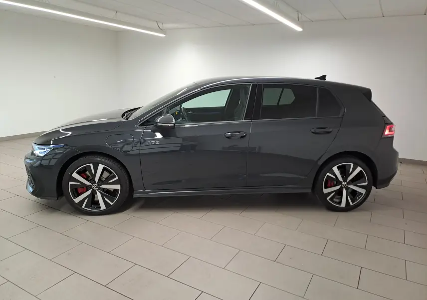 Vue de profil côté gauche d'une Volkswagen Golf 1.5 eHybrid 272 DSG6 GTE gris Urano avec jantes sport et feux arrière allumés.