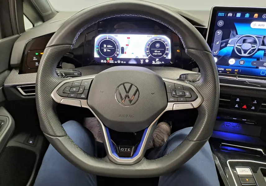 Vue intérieure centrée sur le volant perforé de la Volkswagen Golf 1.5 eHybrid 2025 avec logo GTE et tableau de bord numérique.