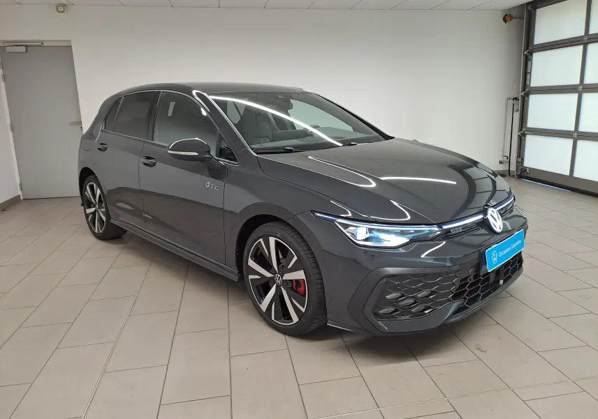 Volkswagen Golf 1.5 eHybrid gris Urano vue 3/4 avant droit, avec badge GTE et jantes sport bicolores.