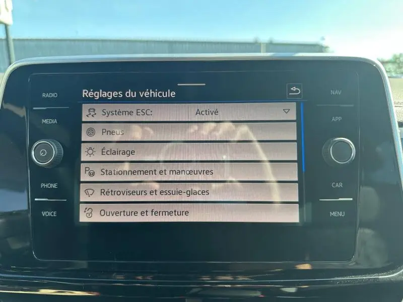 Écran tactile central du Volkswagen T-Roc noir nacré affichant les réglages du véhicule en plein jour.