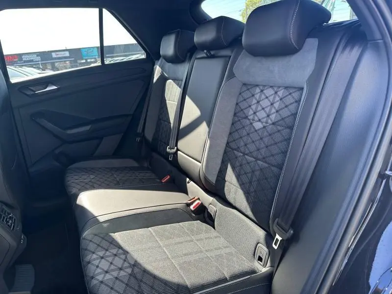 Vue intérieure côté arrière droit du Volkswagen T-Roc 2025, sièges en artvelours gris avec motifs géométriques et ceintures noires.