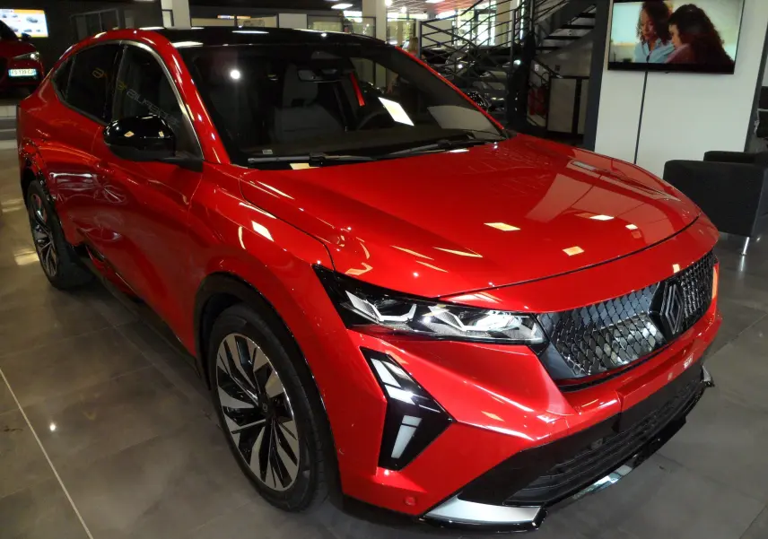 Renault Rafale E-Tech Full Hybrid rouge flamme avec toit noir, vue 3/4 avant en showroom, calandre noire distinctive.