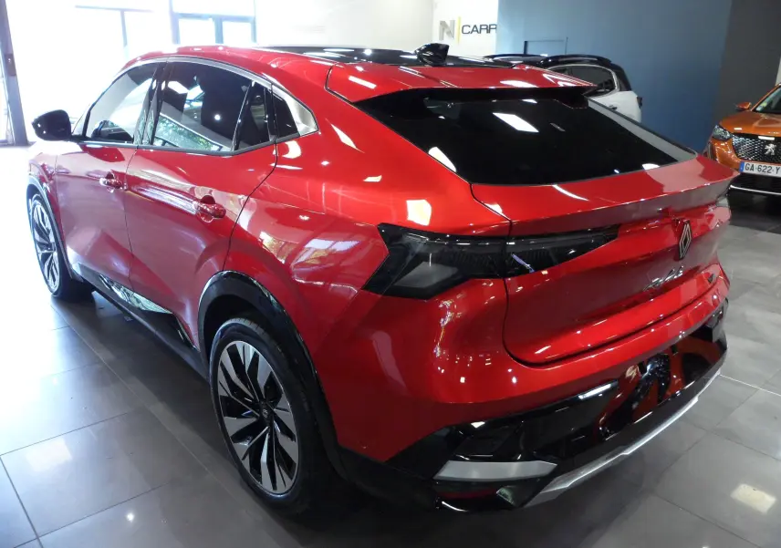 Vue 3/4 arrière droite du Renault Rafale E-Tech hybride rouge flamme avec toit noir et jantes bicolores en showroom.