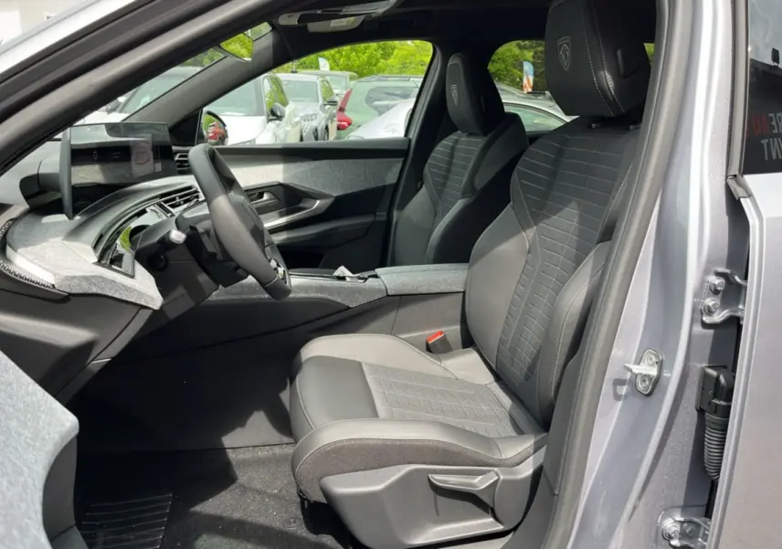 Vue intérieure côté conducteur du Peugeot 3008 Hybrid 145 gris titane, mettant en valeur les sièges en tissu et cuir avec logo Peugeot brodé.