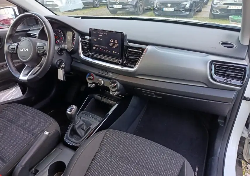 Vue 3/4 arrière droite d’un KIA Stonic blanc 2022 en showroom, avec toit ouvrant et jantes alliage visibles.