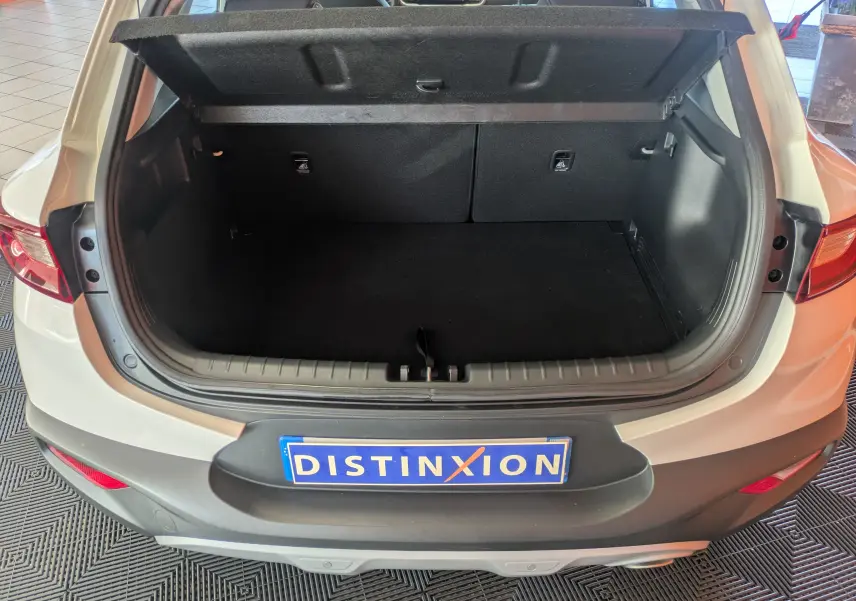 Coffre ouvert vu de l'arrière d'un KIA Stonic blanc 2022, montrant l'espace de chargement et la tablette cache-bagages relevée.