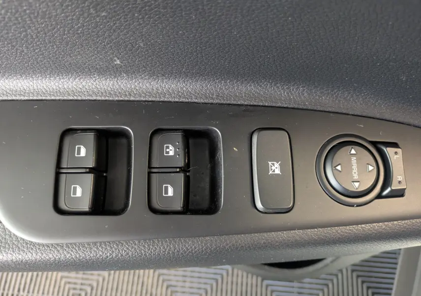 Gros plan sur les commandes de lève-vitres et réglage des rétroviseurs côté conducteur d’un KIA Stonic blanc.
