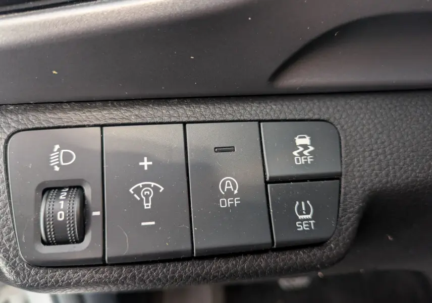 Gros plan sur les commandes noires du tableau de bord du Kia Stonic blanc, avec réglage phares et fonctions de sécurité.