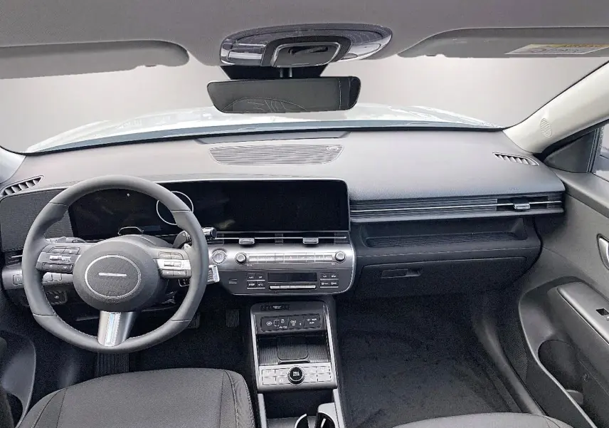 Vue intérieure avant du Hyundai Kona gris 2025, tableau de bord moderne avec écran large et volant multifonction cuir.
