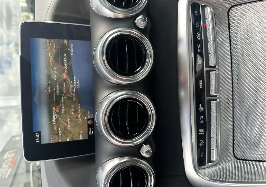 Vue rapprochée du tableau de bord gris foncé d'une Mercedes AMG GT 2015, avec écran GPS et aérateurs ronds chromés.