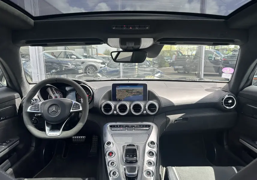Vue intérieure avant de la Mercedes AMG GT 2015 gris foncé, avec volant AMG, tableau de bord et console centrale en carbone.