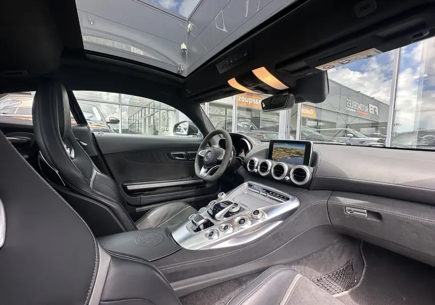 Vue intérieure côté conducteur du Mercedes AMG GT 2015 gris foncé, avec console centrale alu et toit panoramique.