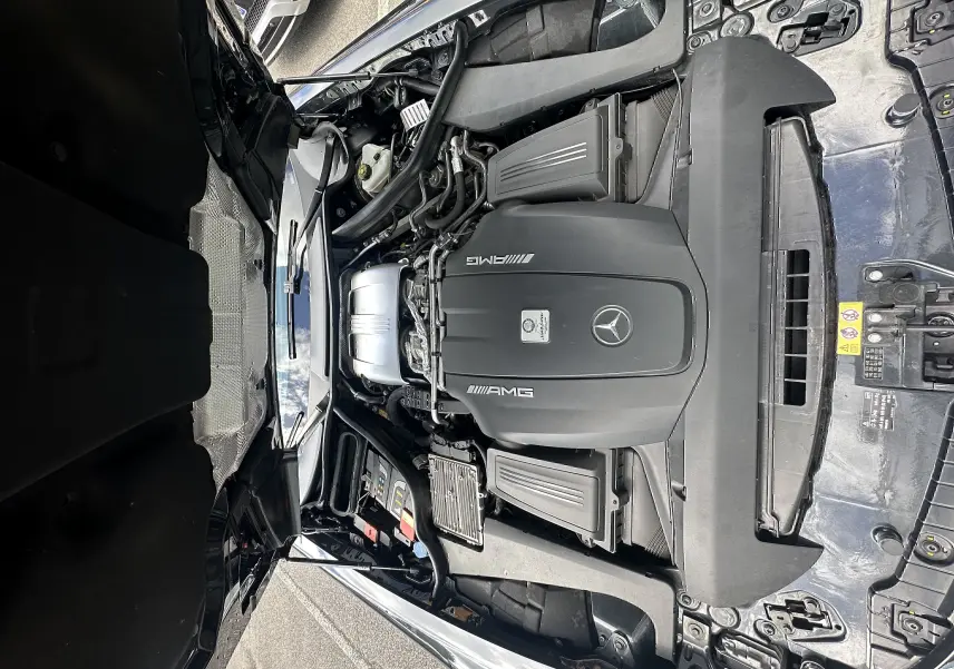 Moteur AMG V8 visible sous le capot ouvert d'une Mercedes AMG GT gris foncé, vue de dessus en extérieur.