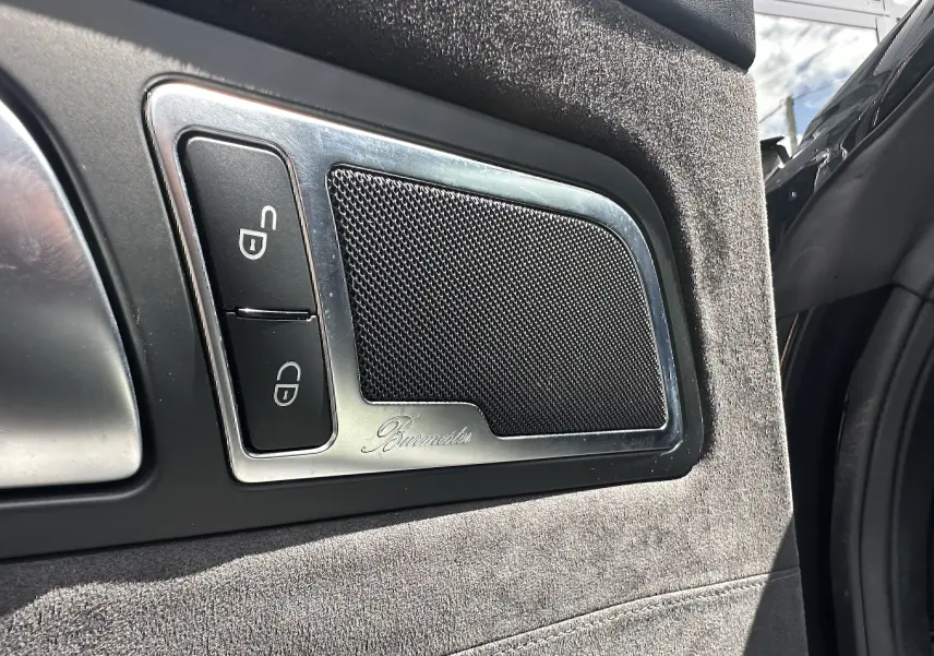 Détail intérieur côté gauche de la porte d’une Mercedes AMG GT 2015 gris foncé, avec haut-parleur Burmester et boutons de verrouillage.