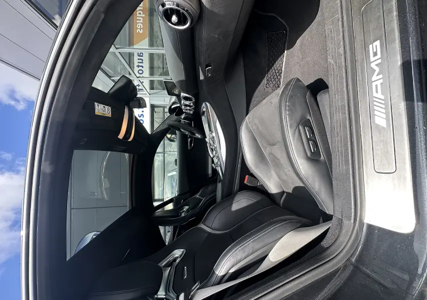 Vue intérieure côté conducteur de la Mercedes AMG GT 2015, sièges en cuir noir et seuil de porte AMG visible.