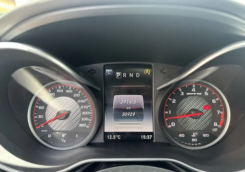 Tableau de bord du Mercedes AMG GT 2015, affichage digital central et compteurs avec fond carbone, vue frontale rapprochée.