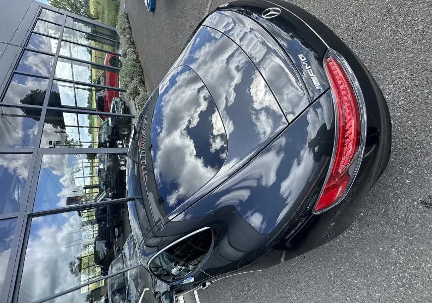 Vue arrière en 3/4 d'une Mercedes AMG GT gris foncé brillant, avec feux arrière allongés et logo AMG visible.