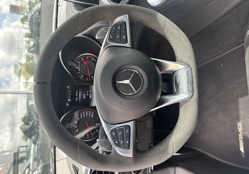 Vue intérieure centrée sur le volant AMG en alcantara noir avec logo Mercedes et tableau de bord du Mercedes AMG GT 2015.