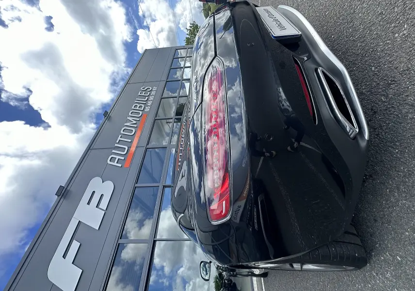 Vue 3/4 arrière droite d'une Mercedes AMG GT gris foncé, avec feux arrière allongés et double sortie d'échappement chromée.