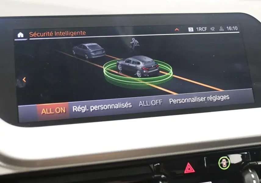 Écran central de la BMW Série 1 16d 2023 montrant l'interface de sécurité intelligente avec vue virtuelle du véhicule noir en circulation.