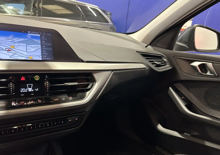 Vue intérieure côté passager de la BMW Série 1 16d noire 2023, avec écran GPS et tableau de bord moderne.