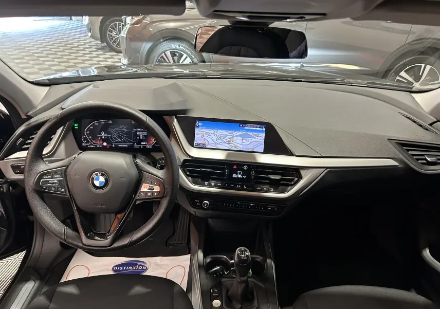 Vue intérieure avant de la BMW Série 1 noire 2023, avec tableau de bord digital et écran GPS intégré.
