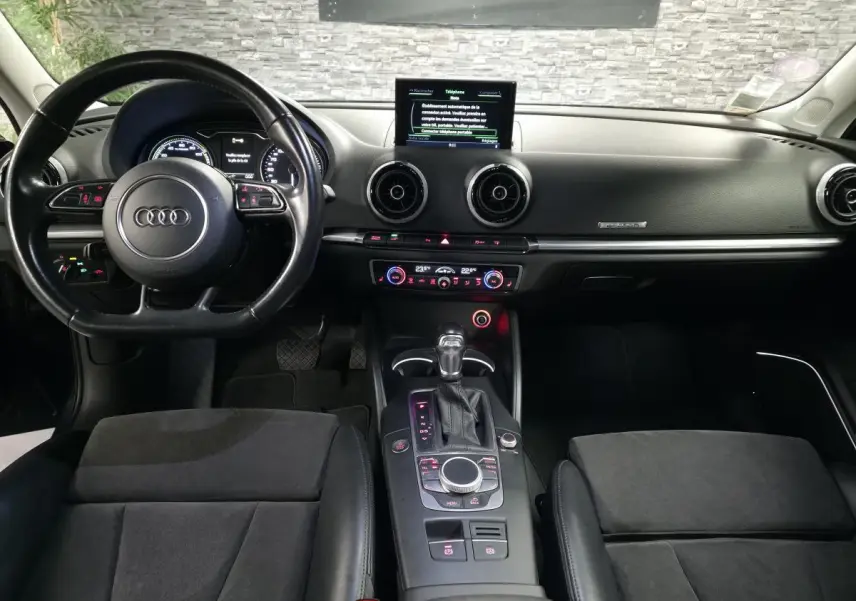 Vue intérieure avant de l'Audi A3 Sportback 2015, tableau de bord noir avec écran central et volant multifonction cuir.