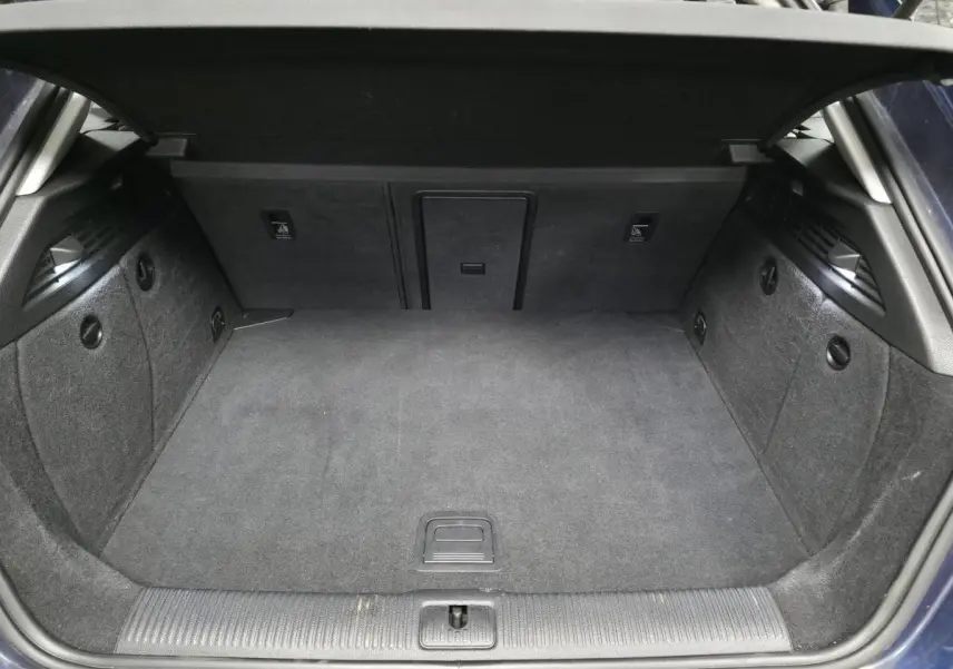 Coffre ouvert en vue arrière d'une Audi A3 Sportback bleu, avec tapis de sol gris et trappe à skis intégrée.
