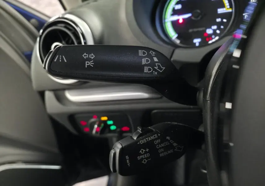 Gros plan sur les commandes au volant côté gauche de l'Audi A3 Sportback bleu, avec indicateurs de feux et régulateur adaptatif.