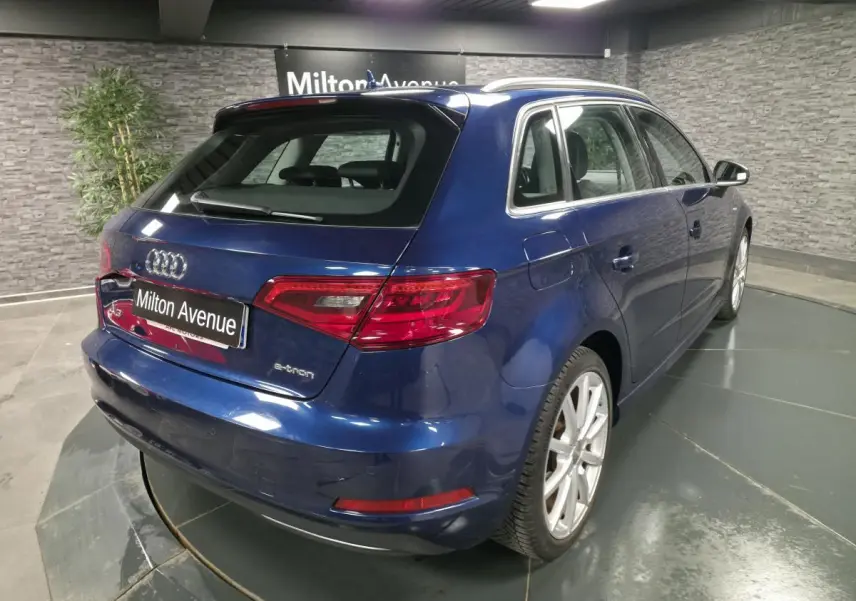 Audi A3 Sportback bleu vue 3/4 arrière droit, avec jantes aluminium et badge e-tron visible sur le coffre.