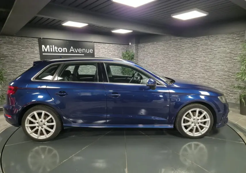 Profil côté gauche d'une Audi A3 Sportback bleu métallisé avec jantes alu 10 branches dans un showroom.