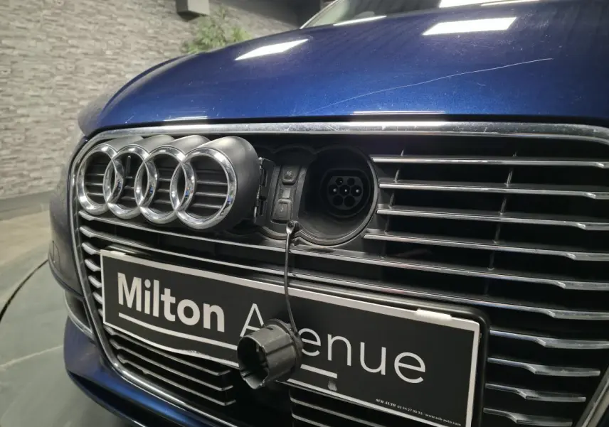 Vue rapprochée avant d'une Audi A3 Sportback bleu avec prise de recharge visible derrière l'emblème Audi ouvert.