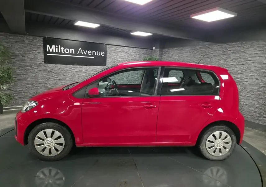 Profil droit d'une Volkswagen Up rouge 2018 avec jantes acier et enjoliveurs VW en aluminium dans un showroom.