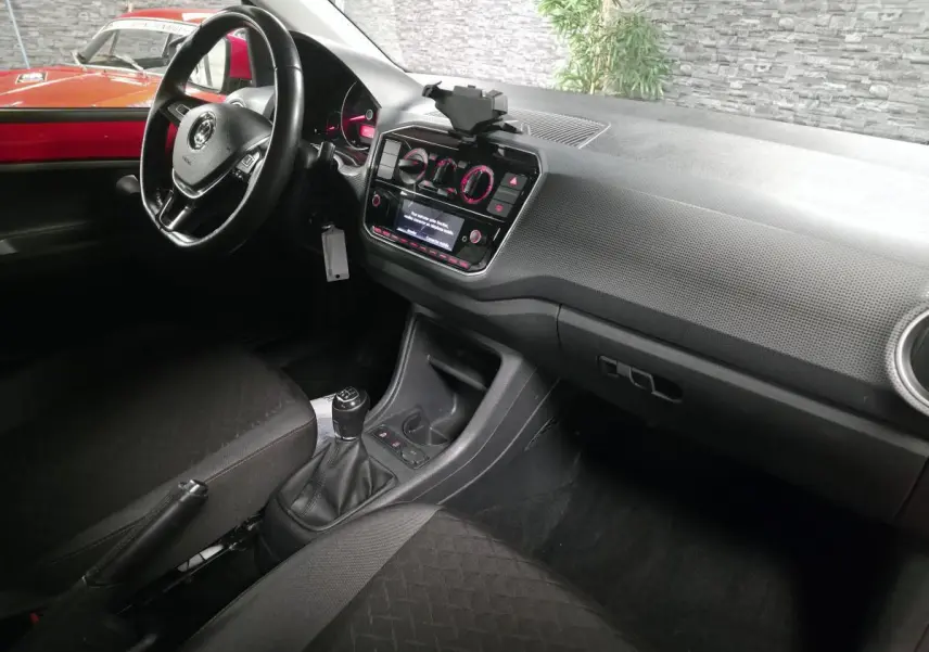 Intérieur avant droit d'une Volkswagen Up rouge, volant cuir multifonctions et levier de vitesses manuel visibles.