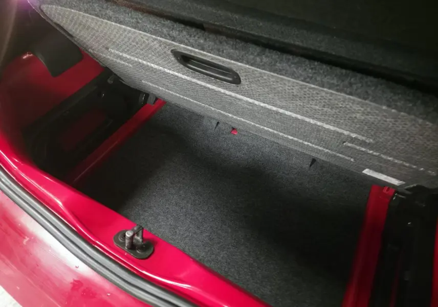 Coffre ouvert vu de dessus d'une Volkswagen Up rouge, montrant le double plancher de chargement en feutre.