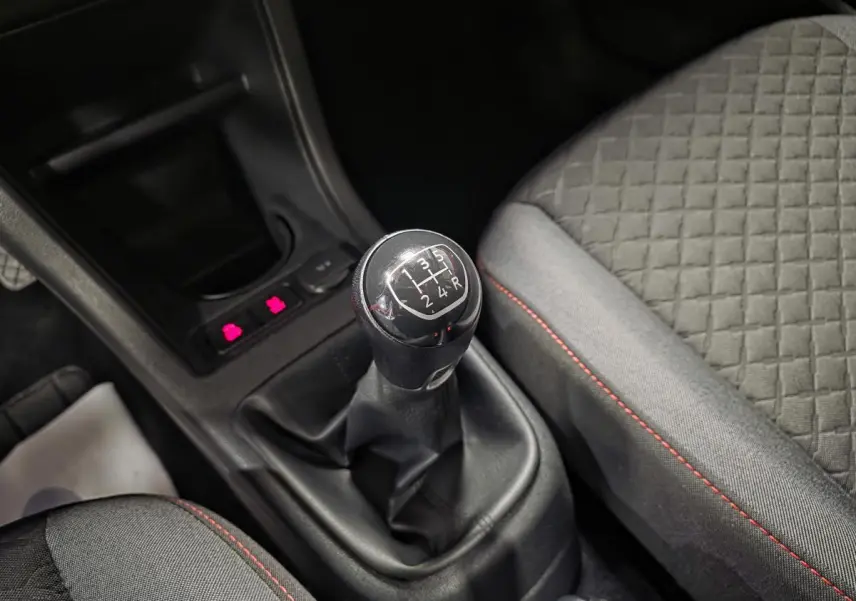 Gros plan sur le levier de vitesses manuel noir et la sellerie grise avec surpiqûres rouges dans une Volkswagen Up rouge.