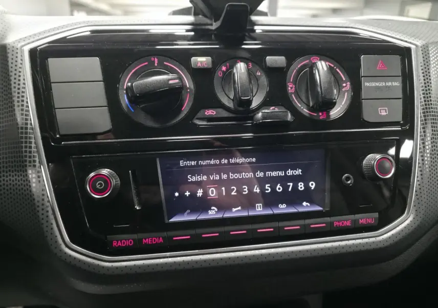 Vue rapprochée de la console centrale noire du Volkswagen Up rouge 2018 avec commandes de climatisation et écran tactile.