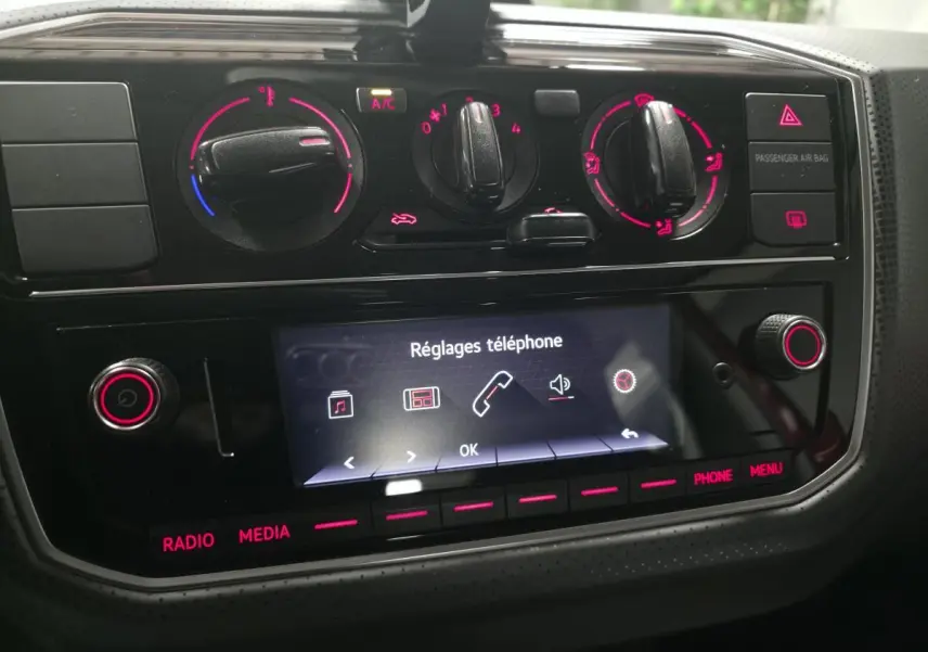 Tableau de bord de Volkswagen UP rouge 2018, vue rapprochée sur commandes climatisation et écran tactile réglages téléphone.