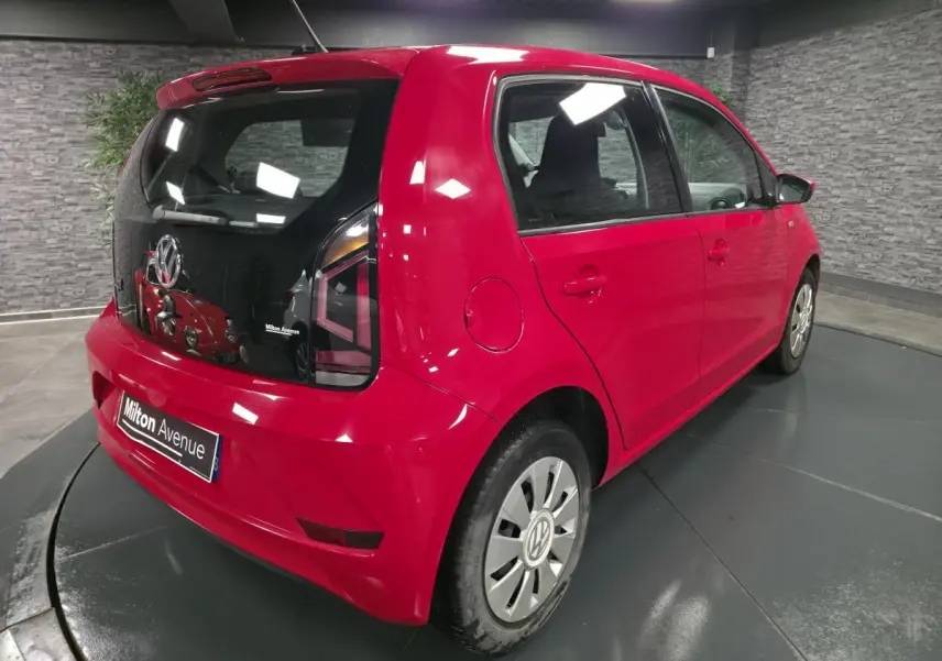 Volkswagen Up rouge vue 3/4 arrière droit avec jantes acier et vitre arrière teintée dans un showroom.