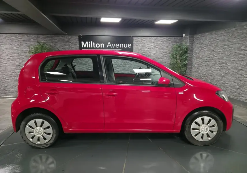 Vue latérale droite d'une Volkswagen Up rouge avec enjoliveurs spécifiques VW et vitres teintées dans un showroom.