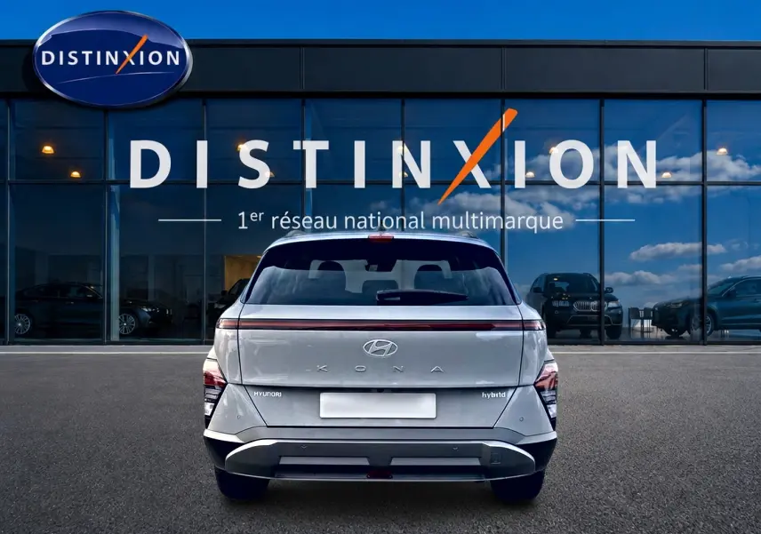 Vue arrière d'un Hyundai Kona gris 2025 avec feux arrière LED et bande lumineuse rouge, devant une vitrine Distinxion.