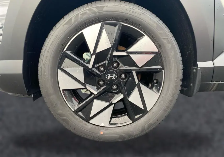 Gros plan sur la roue avant gauche du Hyundai Kona gris 2025 avec jante alliage noire et argentée au design géométrique.