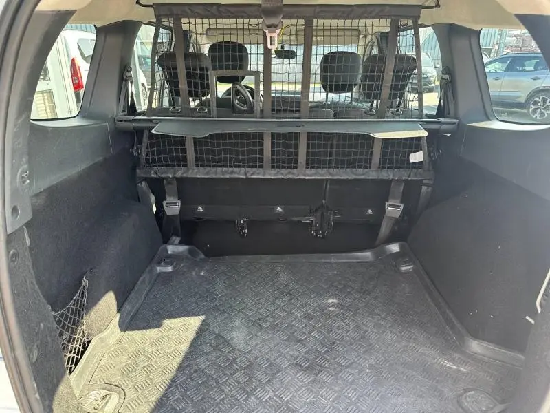 Vue intérieure du coffre du Dacia Lodgy blanc Glacier 2022, avec séparation grillagée et tapis de sol en caoutchouc noir.